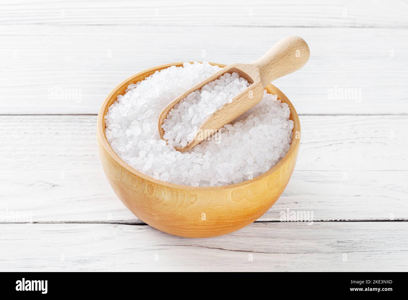 Sea salt in wooden bowl with scoop on white wooden background Stock Photo