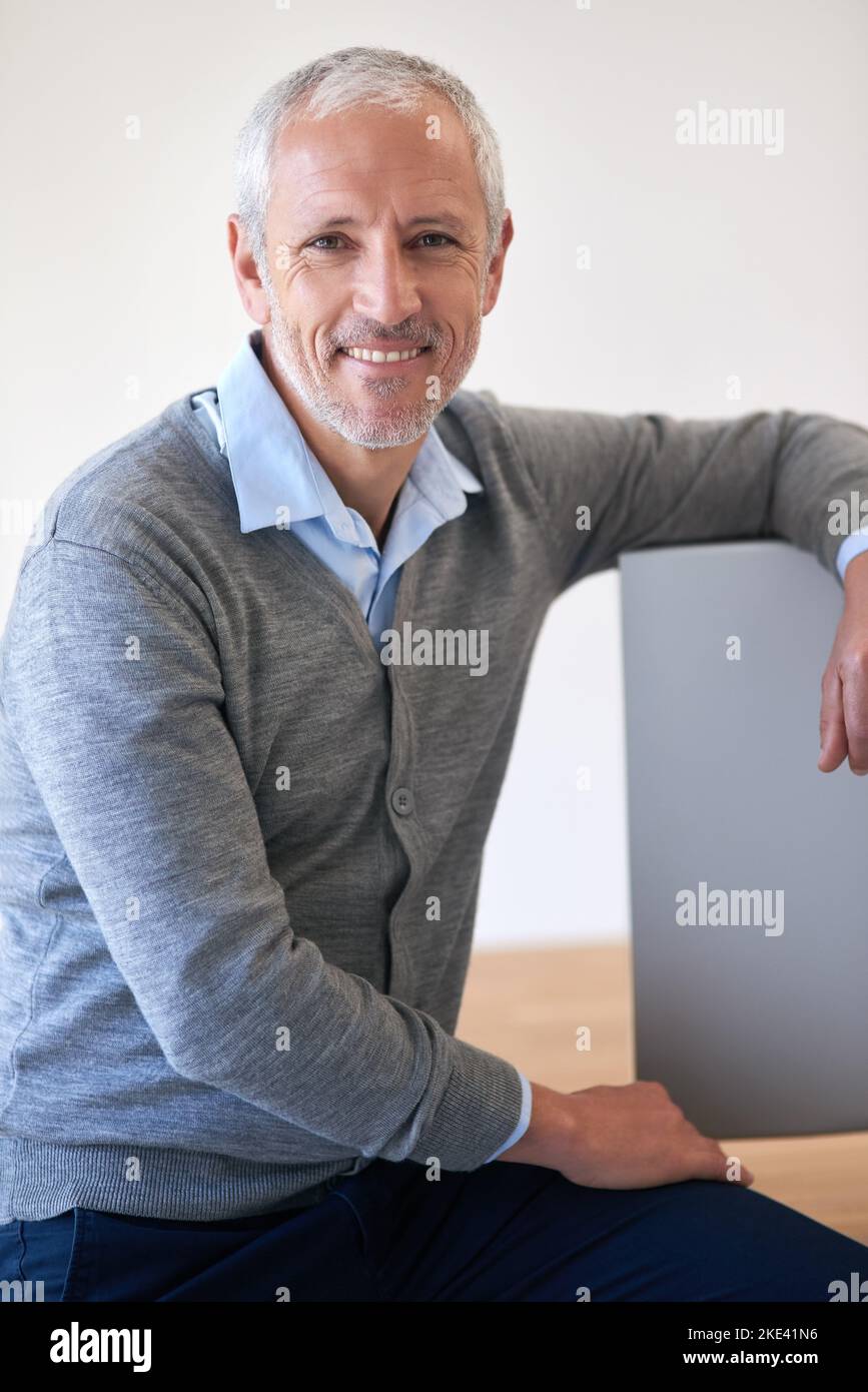 The office life is the life for me. Portrait of a mature businessman leaning on his computer in the office. Stock Photo