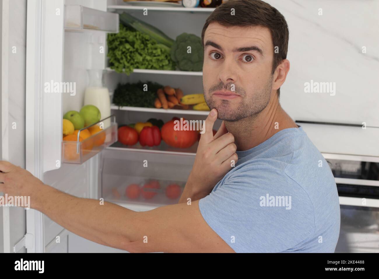 Man opening refrigerator door with doubts Stock Photo Alamy