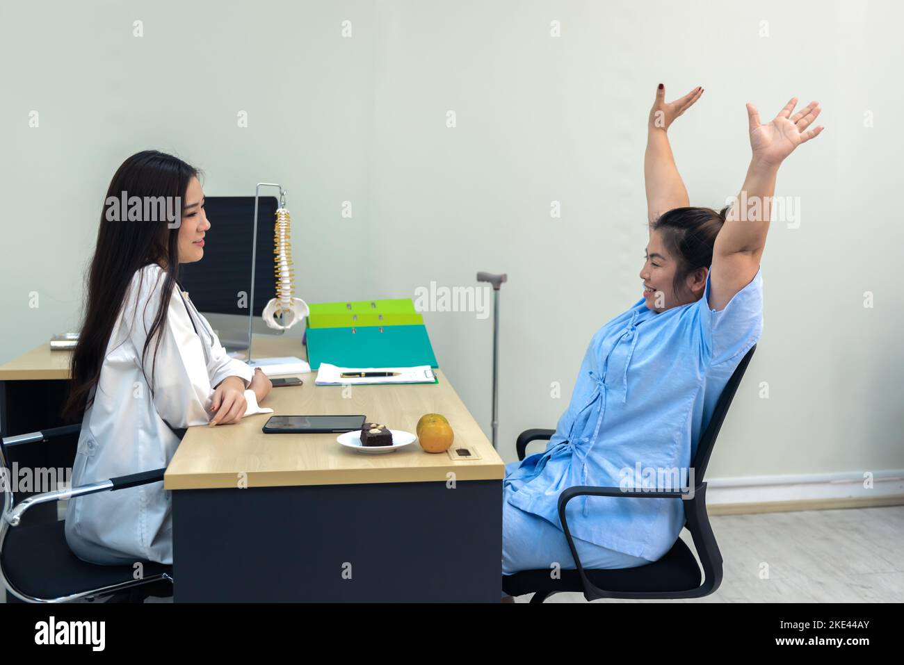 Overweight  Asia woman raised hands and discussing test results with female doctor in hospital, Frozen shoulder concept. Stock Photo