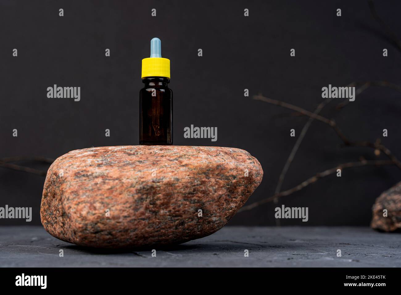 dropper bottle for cosmetics stands on natural stone, black background Stock Photo