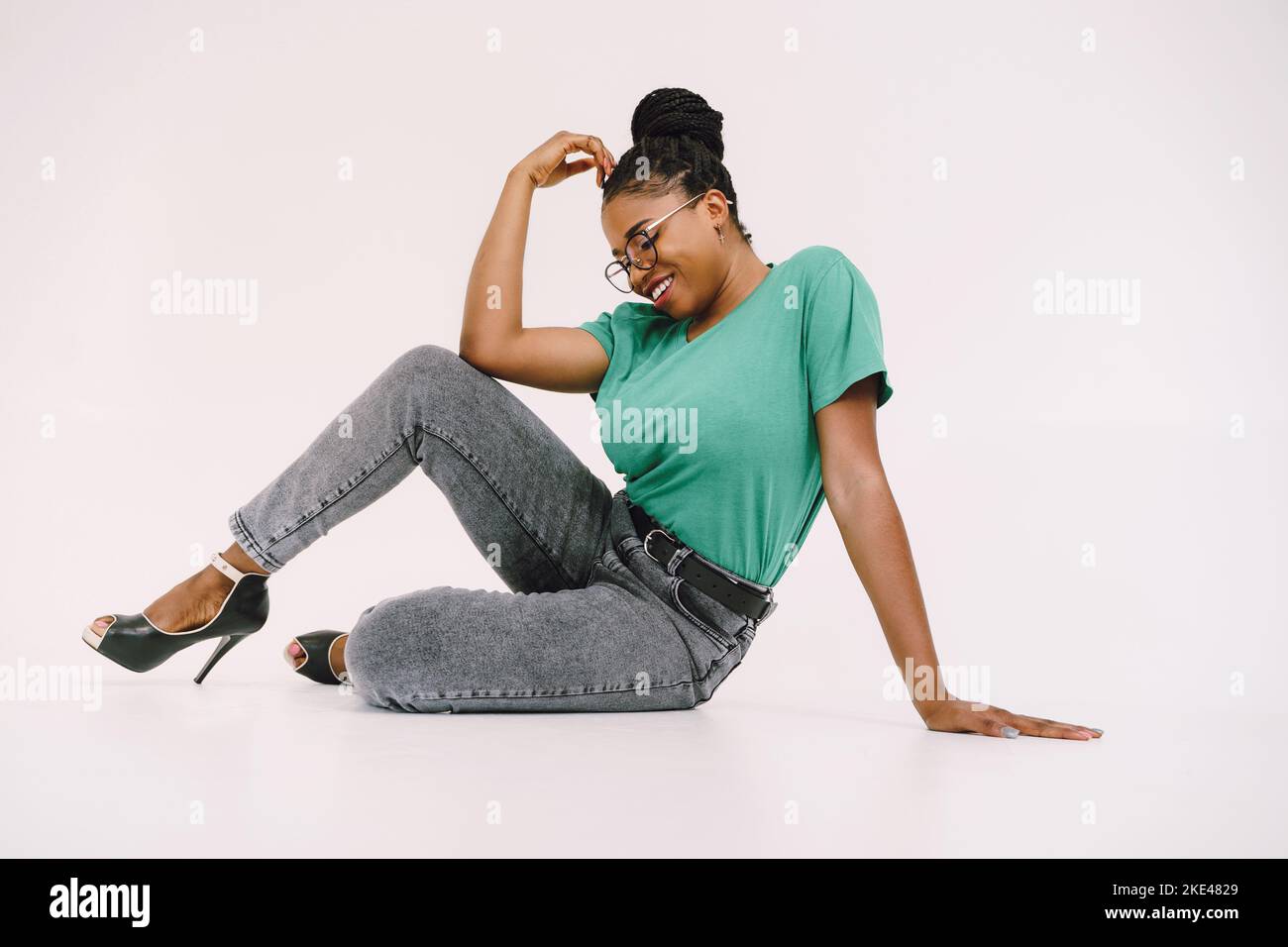 Cheerful African American woman sitting on the floor and smiling on gray background. Studio shot Stock Photo