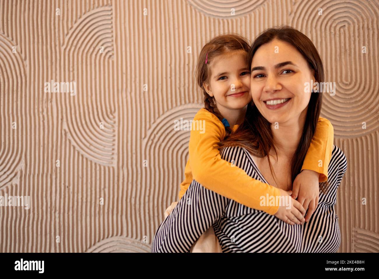 Mom and little daughter hug on beige background with copy space, happy family, parenthood. Concept of maternal love and care Stock Photo