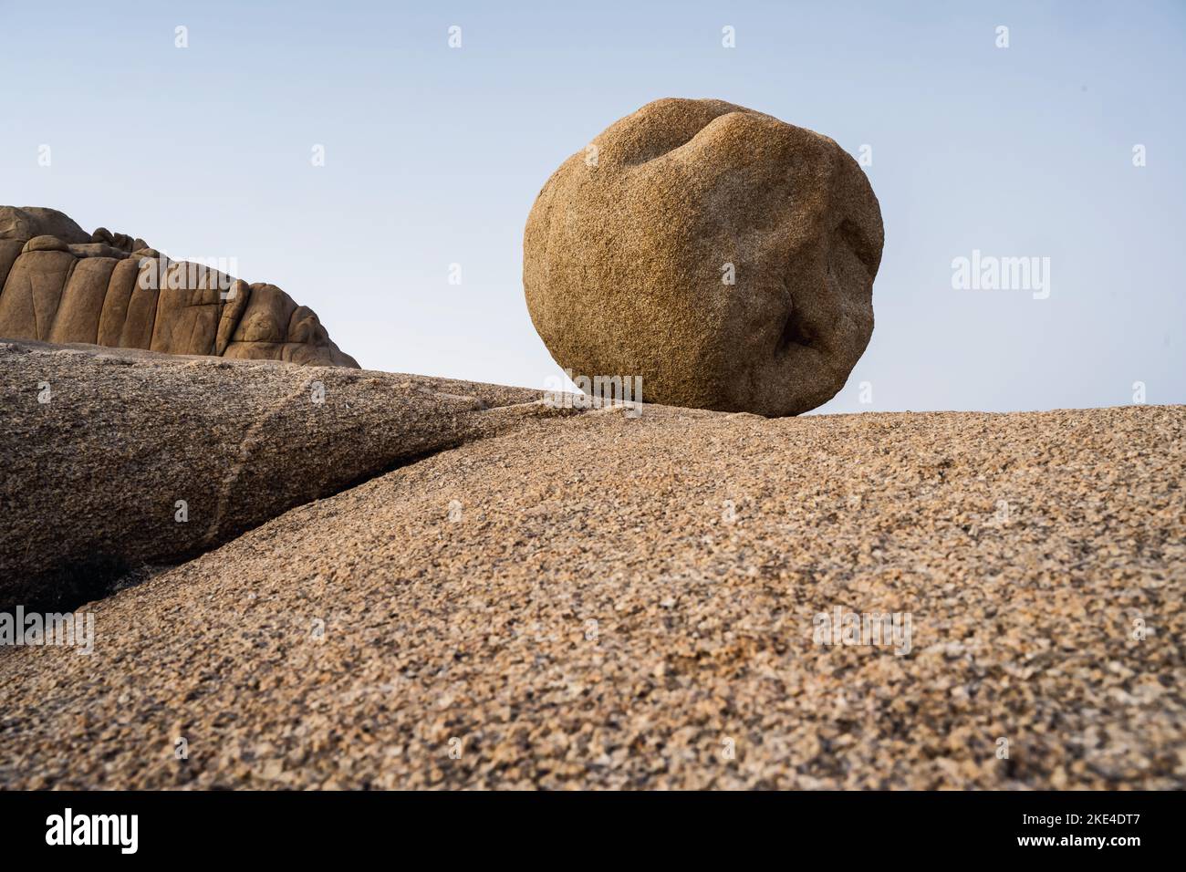 An almost circular rock lies like a ball on a rock plateau against a blue sky. Stock Photo