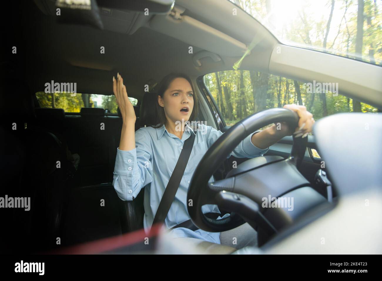 Fright face woman driving car, wide open mouth eyes, strongly squeezing wheel, front window view