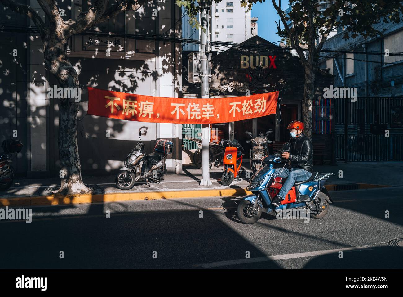 A man driving a scooter in the streets of the old neighborhoods of Shanghai's Former French Concession with a sign in the background Stock Photo