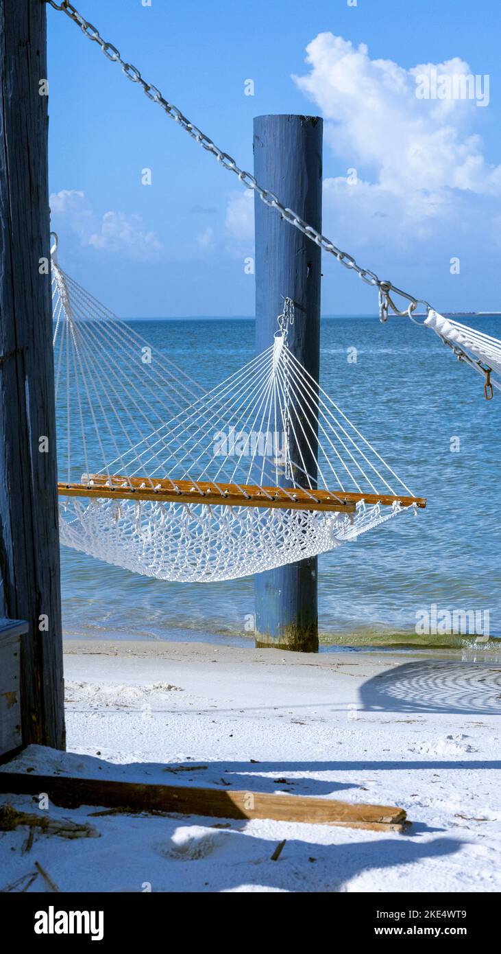 A vertical shot of a hammock on a beach in Gulfport, Mississippi with blue sea and peaceful sky in the background Stock Photo