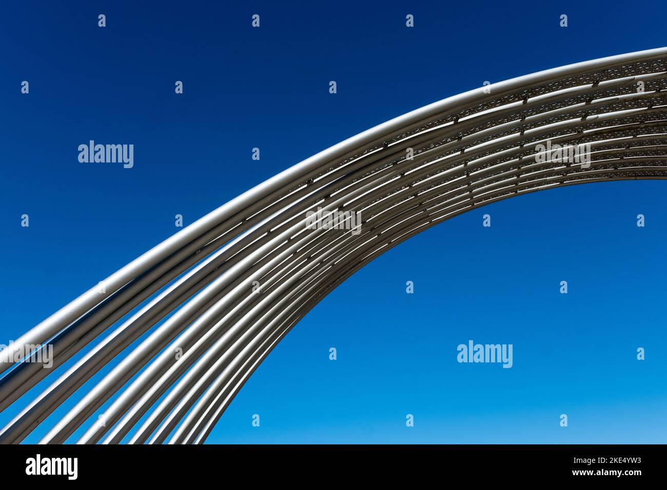 Metal tubes in public space arching in front of clear, deep blue sky ...