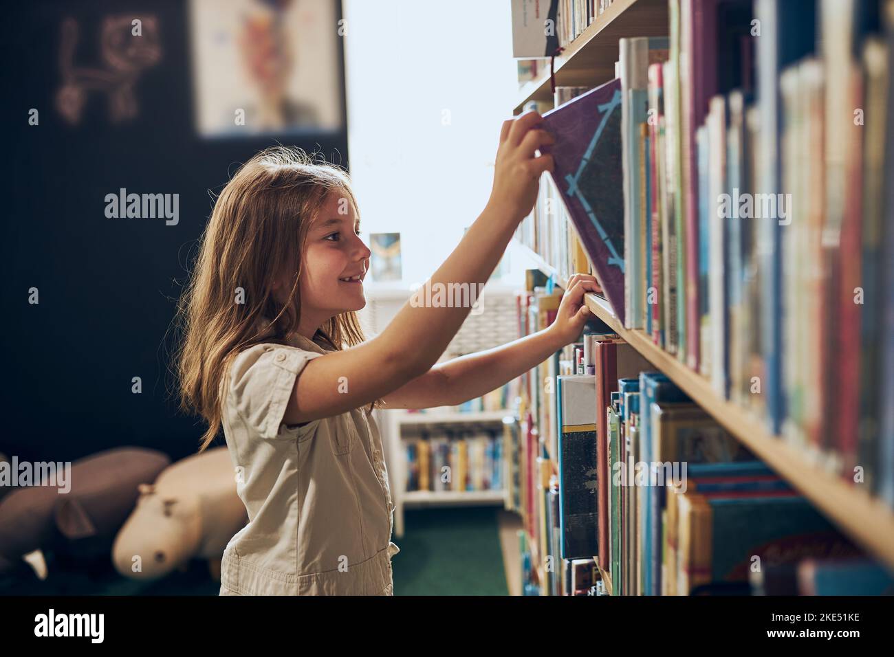 Schoolgirl choosing book in school library. Smart girl selecting