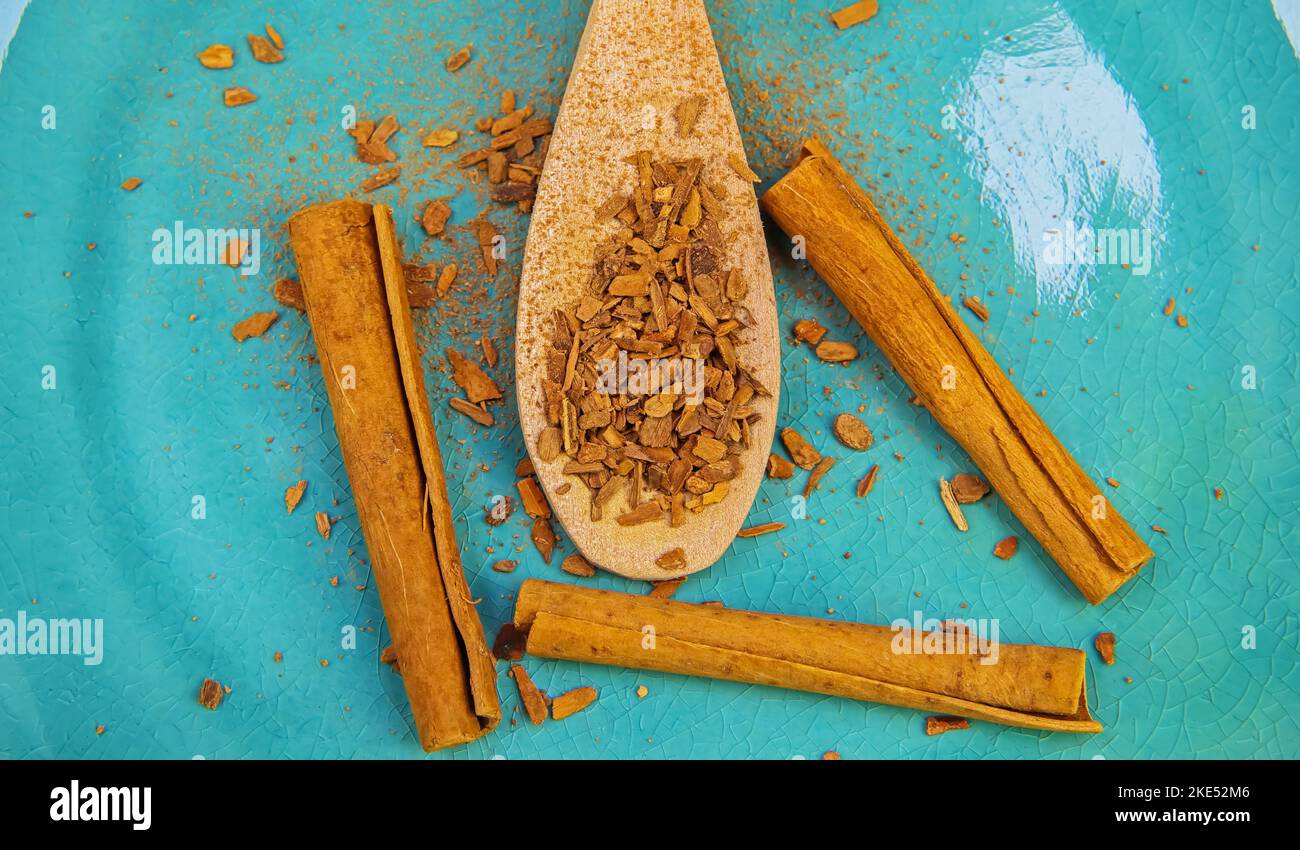 Closeup of isolated wood spoon with natural cinnamon powder, sticks and crumbles on blue scratched china plate Stock Photo