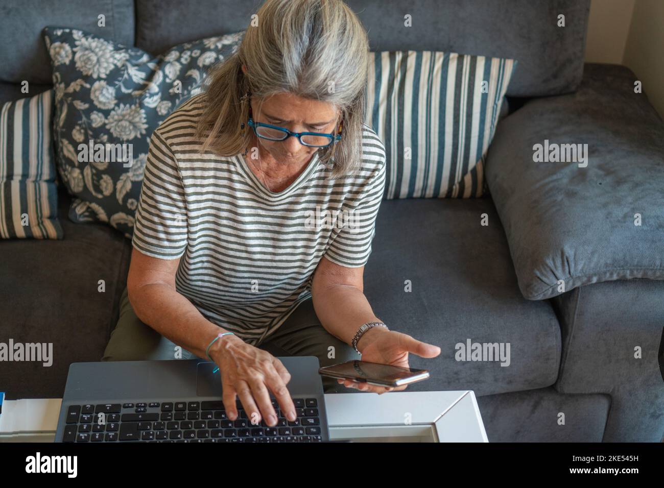 mature woman using cell phone and laptop at home Stock Photo