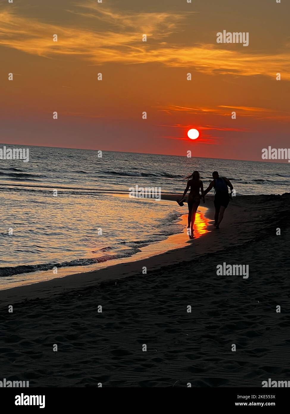 A vertical of a couple silhouette holding hands, walking on the beach ...