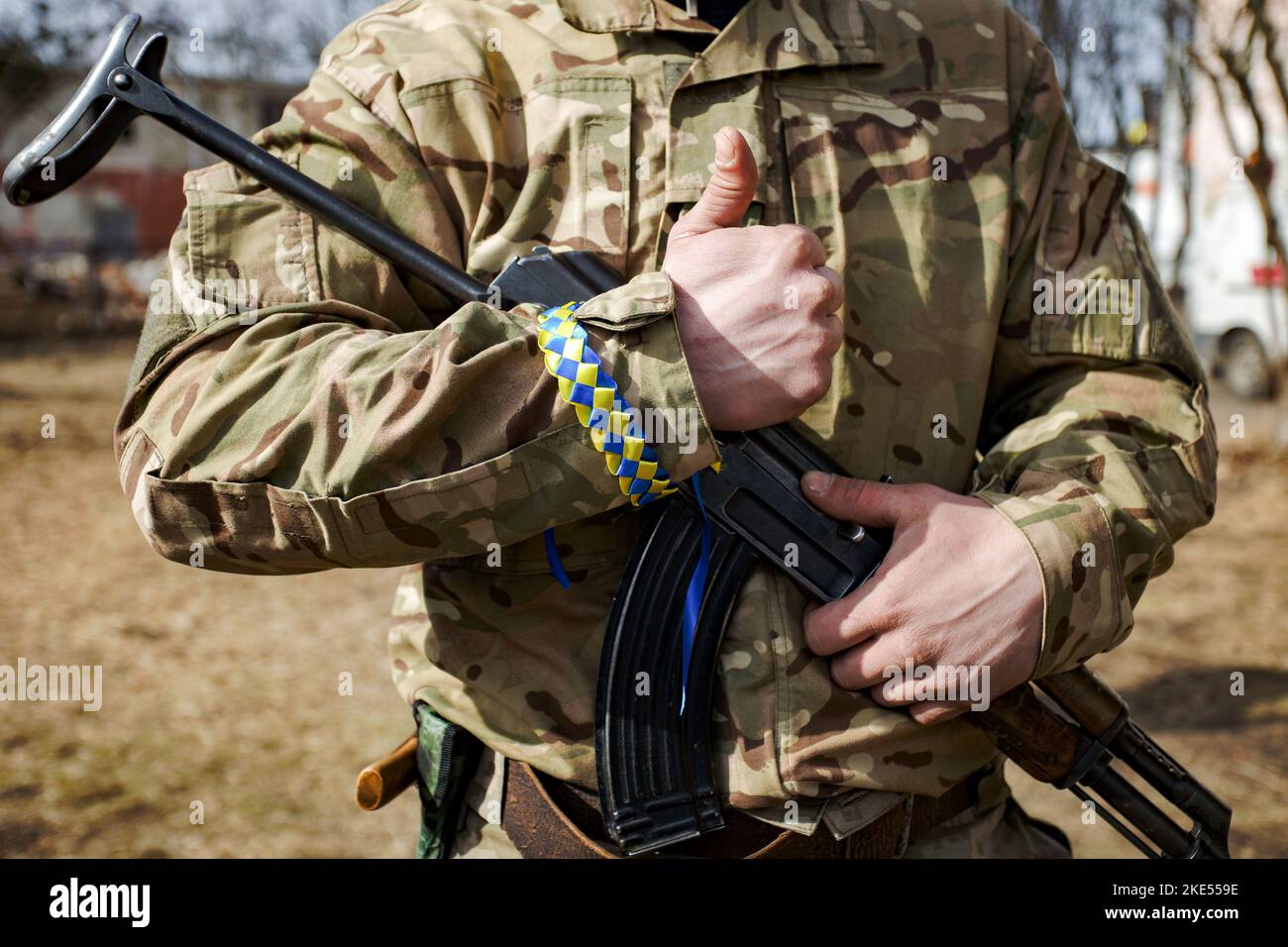The man in camouflage with yellow and blue ribbon wristlet on his hand holding automatic Kalashnikov rifle Stock Photo