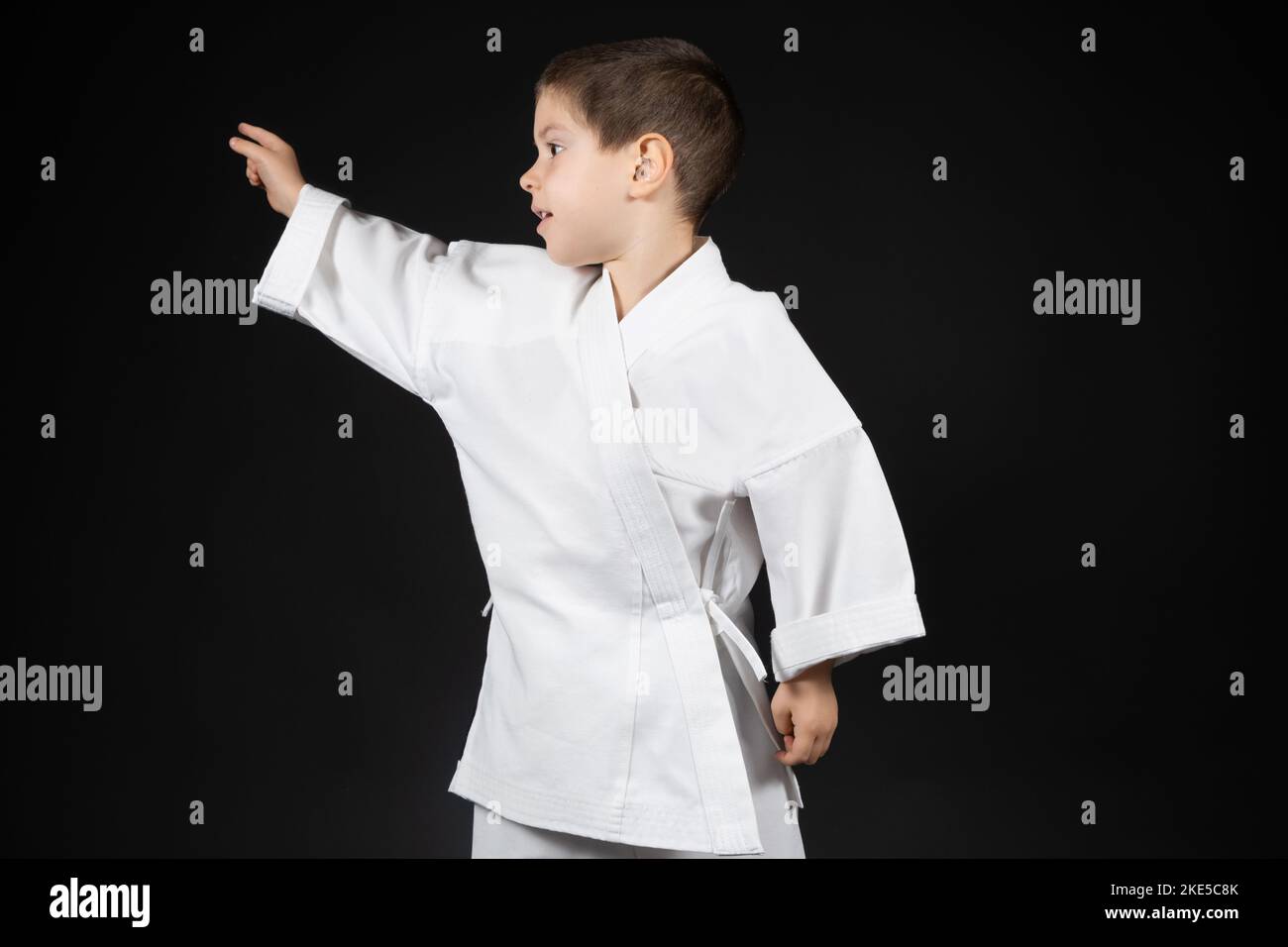 A little boy in a kimono points his hand to the side on a black background. Stock Photo