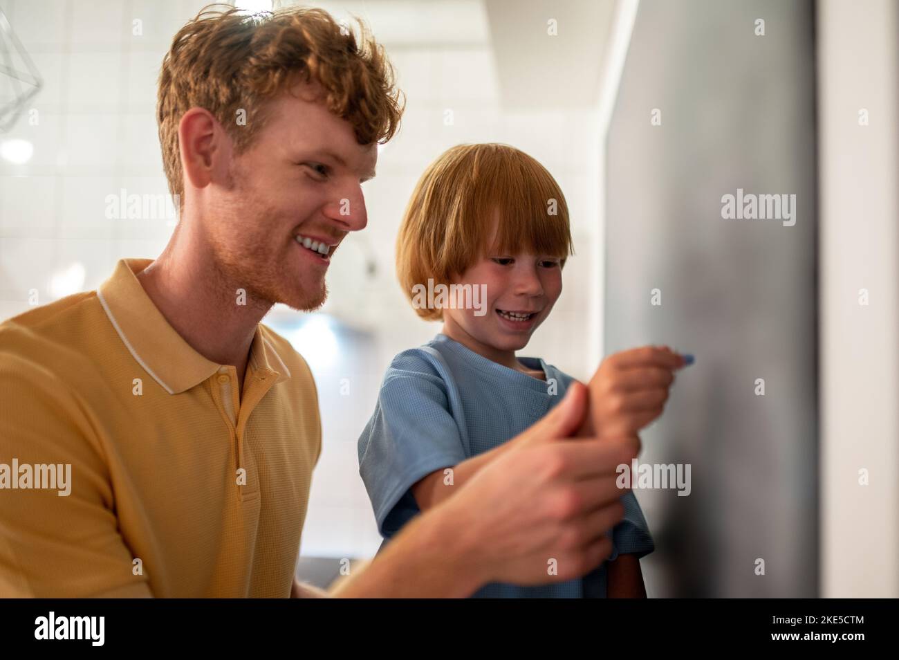 Dad teaching a little boy to write on the blackboard Stock Photo