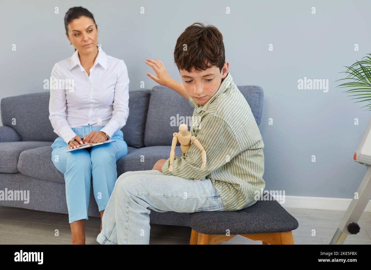 Upset preteen boy turns away and refuses to communicate in therapy session with psychologist. Stock Photo