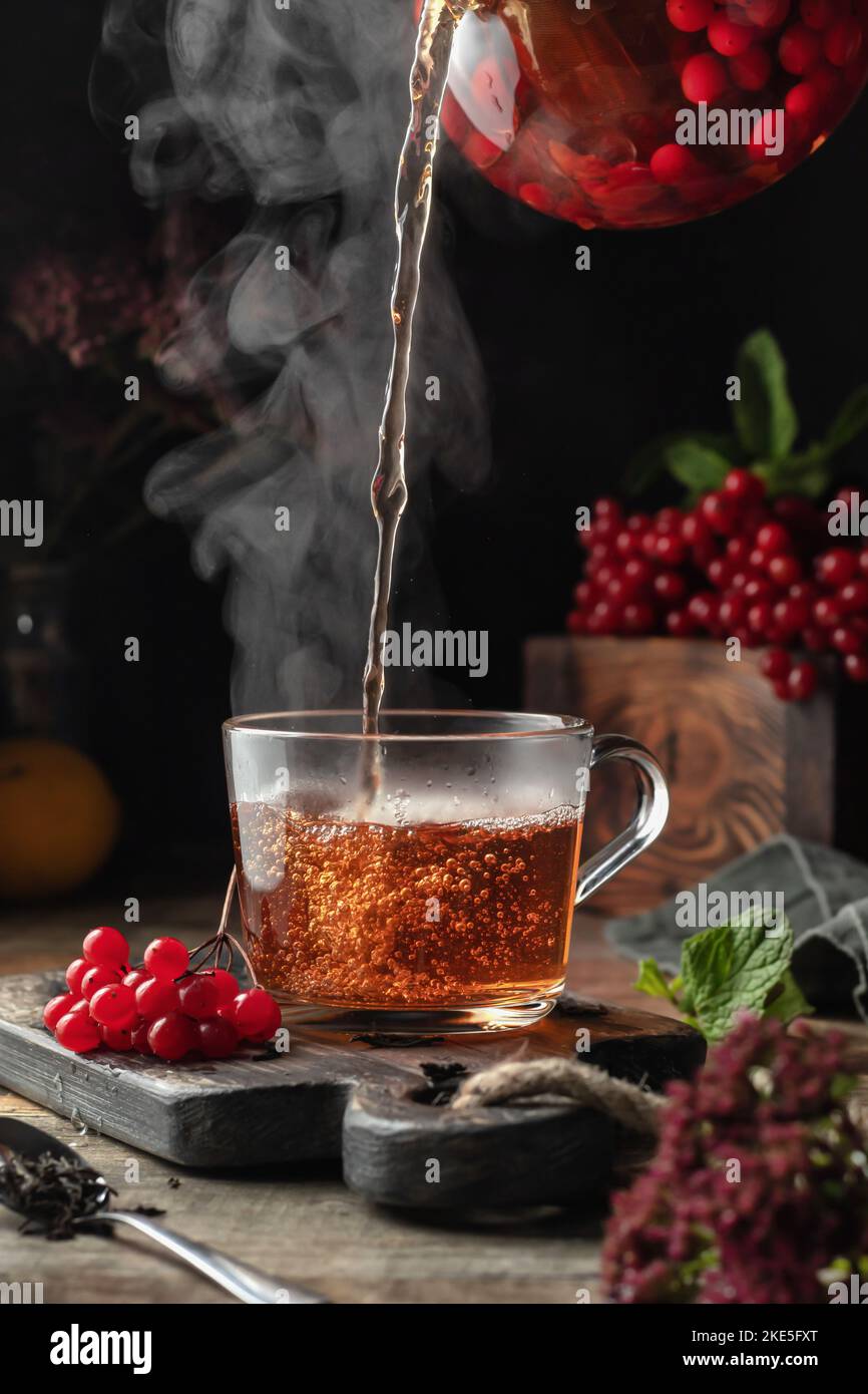 Viburnum tea is poured into a cup with steam, pouring process. Autumn ...