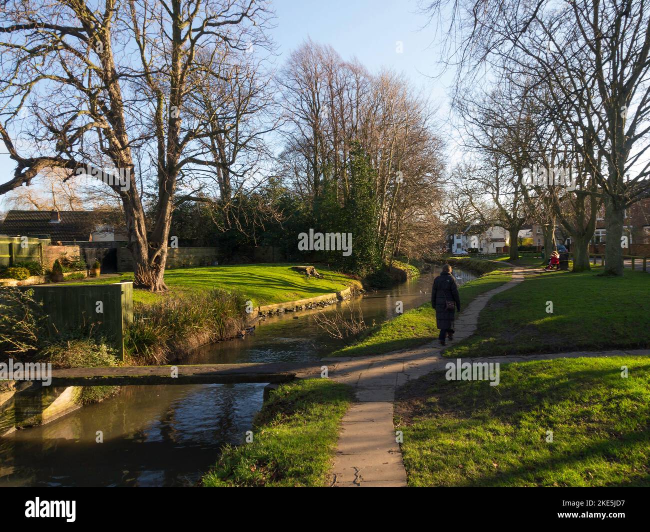A senior woman enjoying a walk on a footpath by the river Leven in Stokesley town centre on a sunny winters day Stock Photo