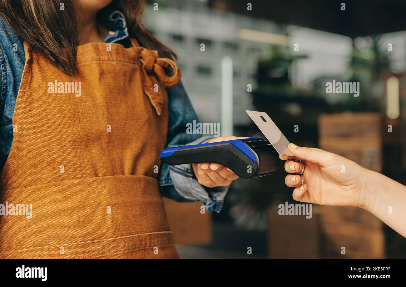 Female customer scanning her credit card on a card machine to pay her bill in a cafe. Unrecognizable woman doing a cashless and contactless transactio Stock Photo