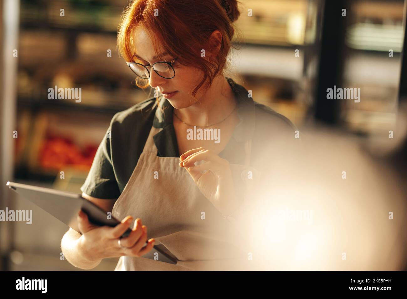 Shop owner taking inventory using a digital tablet in her grocery store. Young female entrepreneur running her small business using wireless technolog Stock Photo