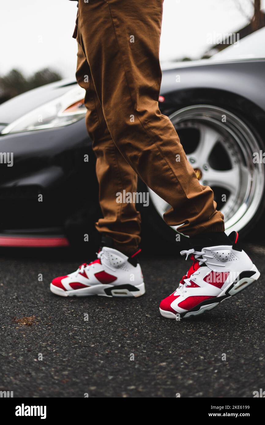 A vertical shot of a male wearing red Jordan 6 carmine sneakers with a car  in the background Stock Photo - Alamy