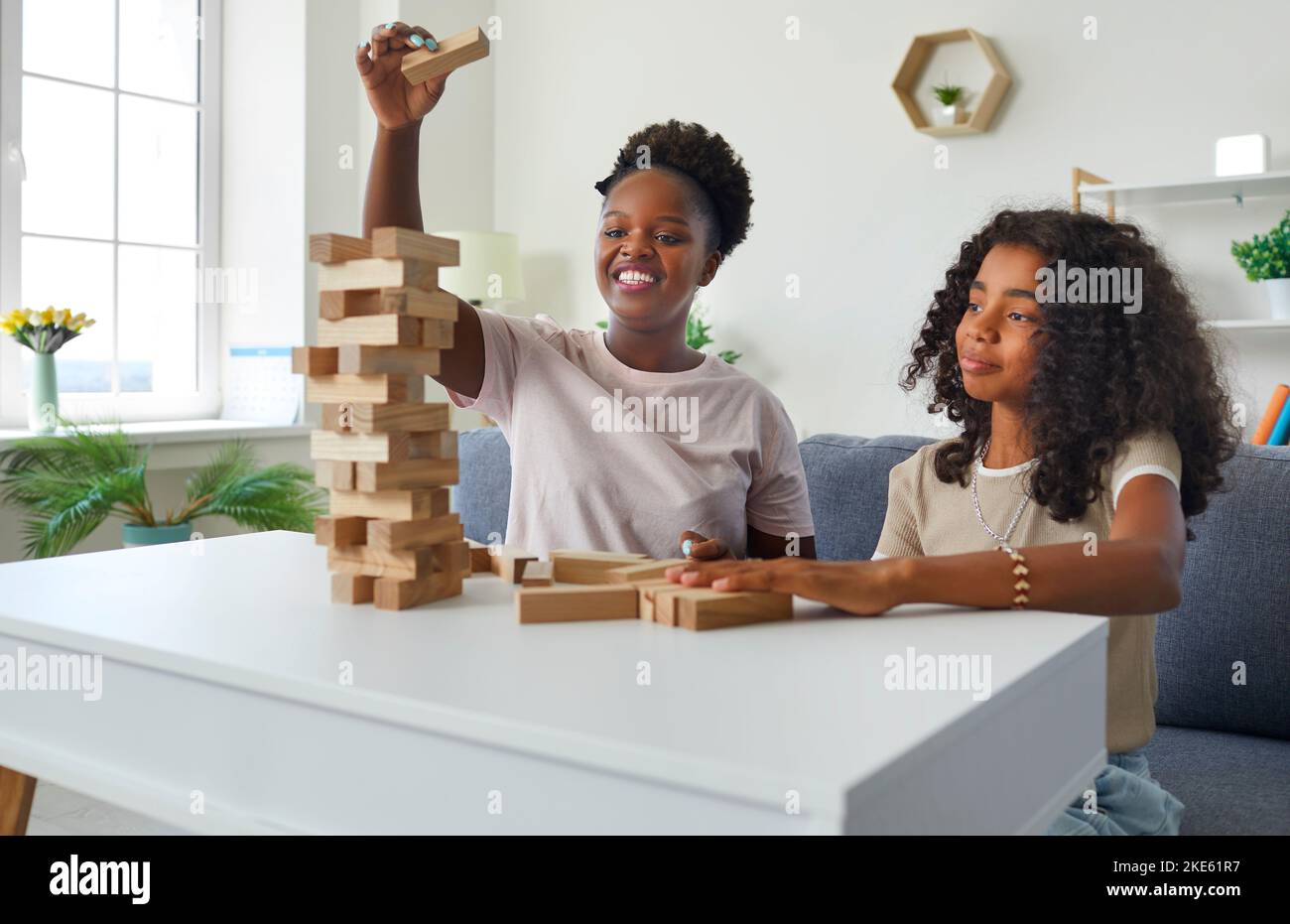 Laughing afroamerican woman psychologist playing tumbling tower with teen girl on therapy session. Stock Photo