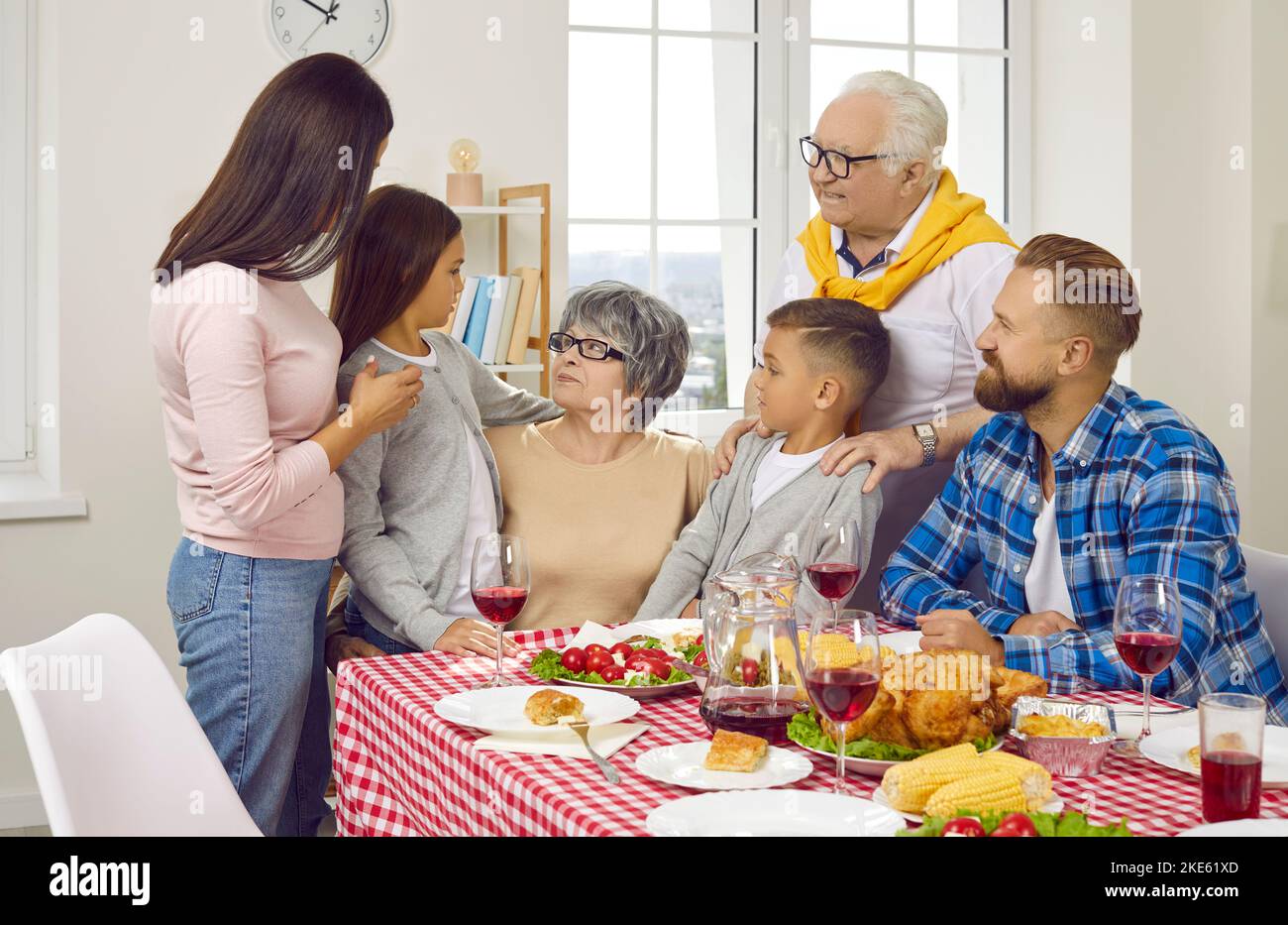 Big family congratulates granny, they are hugging during family dinner at table in living room. Stock Photo
