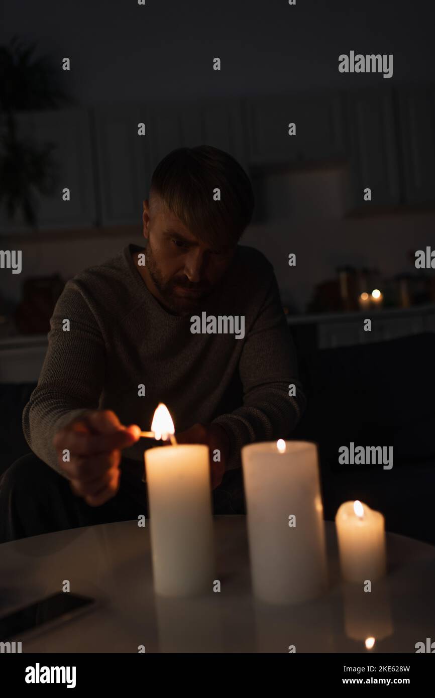 man sitting in dark kitchen during power outage and lighting candles