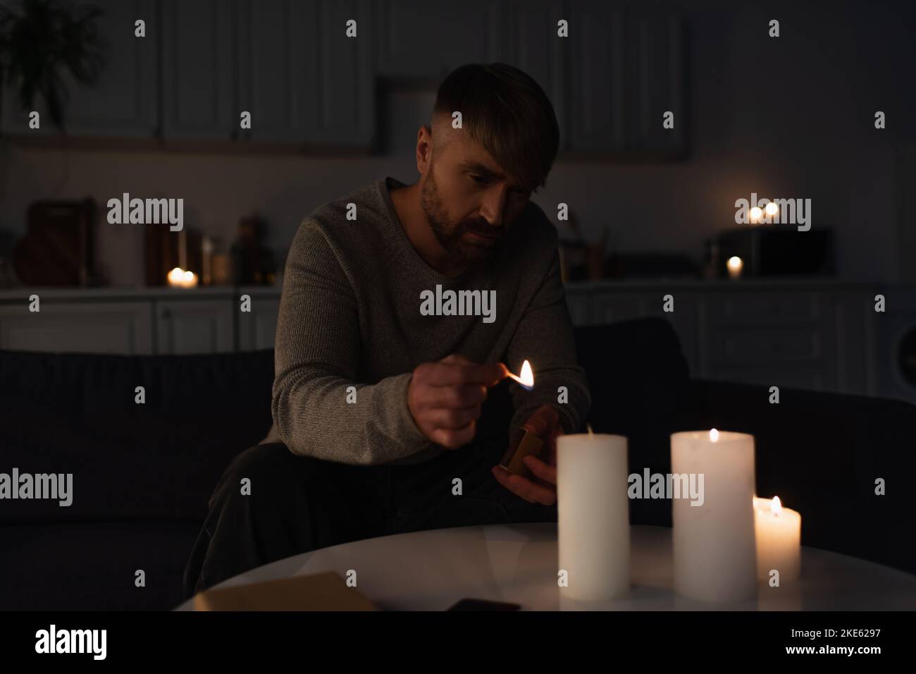 man holding burning match while lighting candles in dark kitchen during