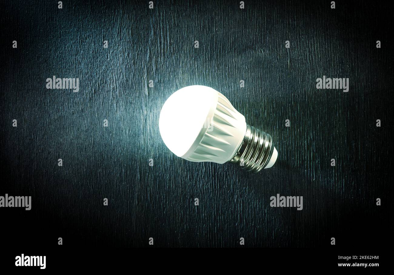Luminous LED lamp on a dark wooden background. Energy saving technology. Stock Photo