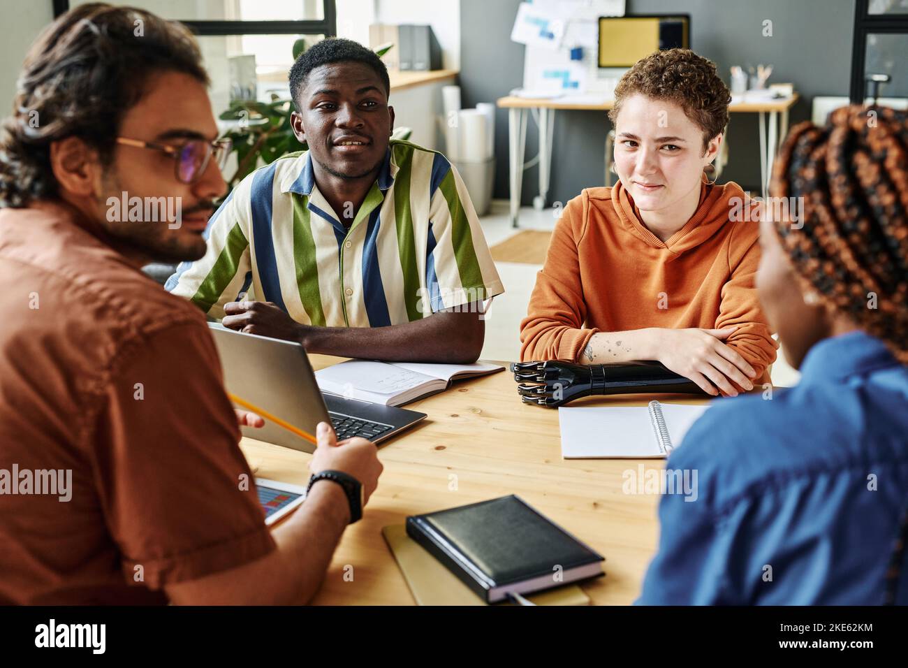 Young creative designer with myoelectric arm and African American man listening to their colleague during discussion of new ideas Stock Photo