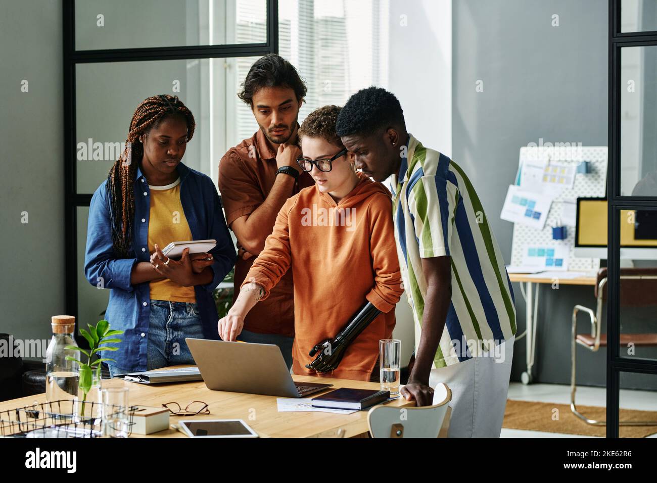 Young confident designer with partial arm pointing at laptop screen while making presentation of project plan to intercultural colleagues Stock Photo