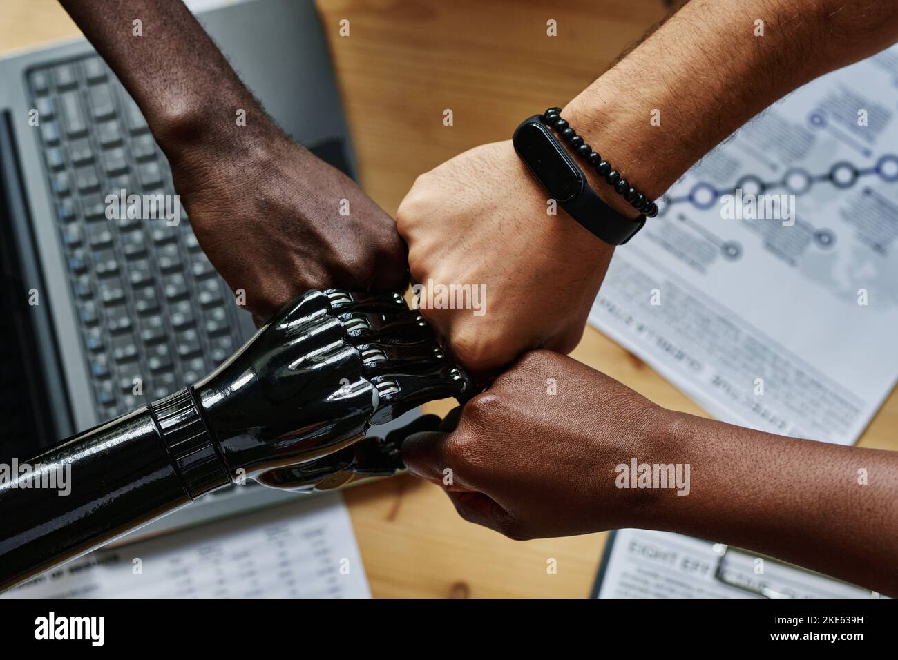 Above shot of hands of young intercultural coworkers including employee with myoelectric arm making punch bump over workplace Stock Photo