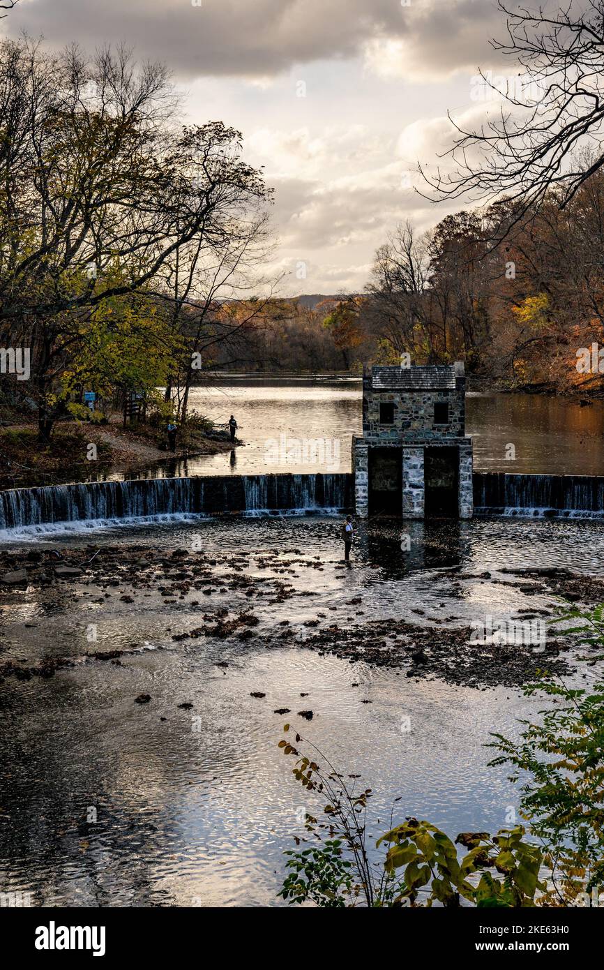 Morristown, NJ - USA - Nov 5, 2022 An autumnal vertical view of New Jersey's historic stone Speedwell Dam during sunset. Fly fisherman in the foregrou Stock Photo