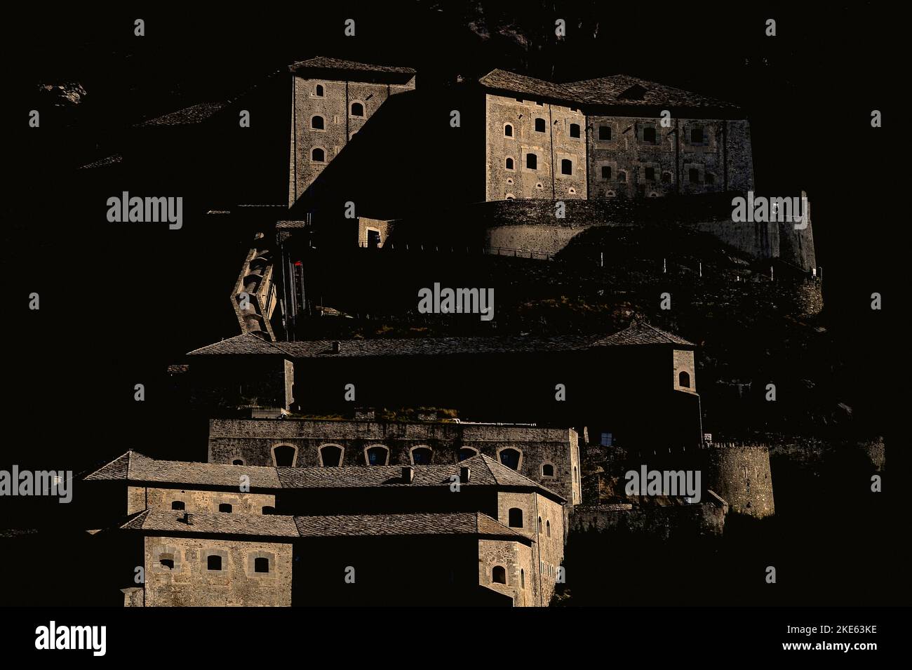 Amid deep shadows, sunlight washes over the walls and gun ports of Fort Bard, an early-19th century Italian bulwark against French invasions built in the steep-sided Aosta Valley gorge at Bard to control the narrow alpine gateway to northwest Italy. Stock Photo