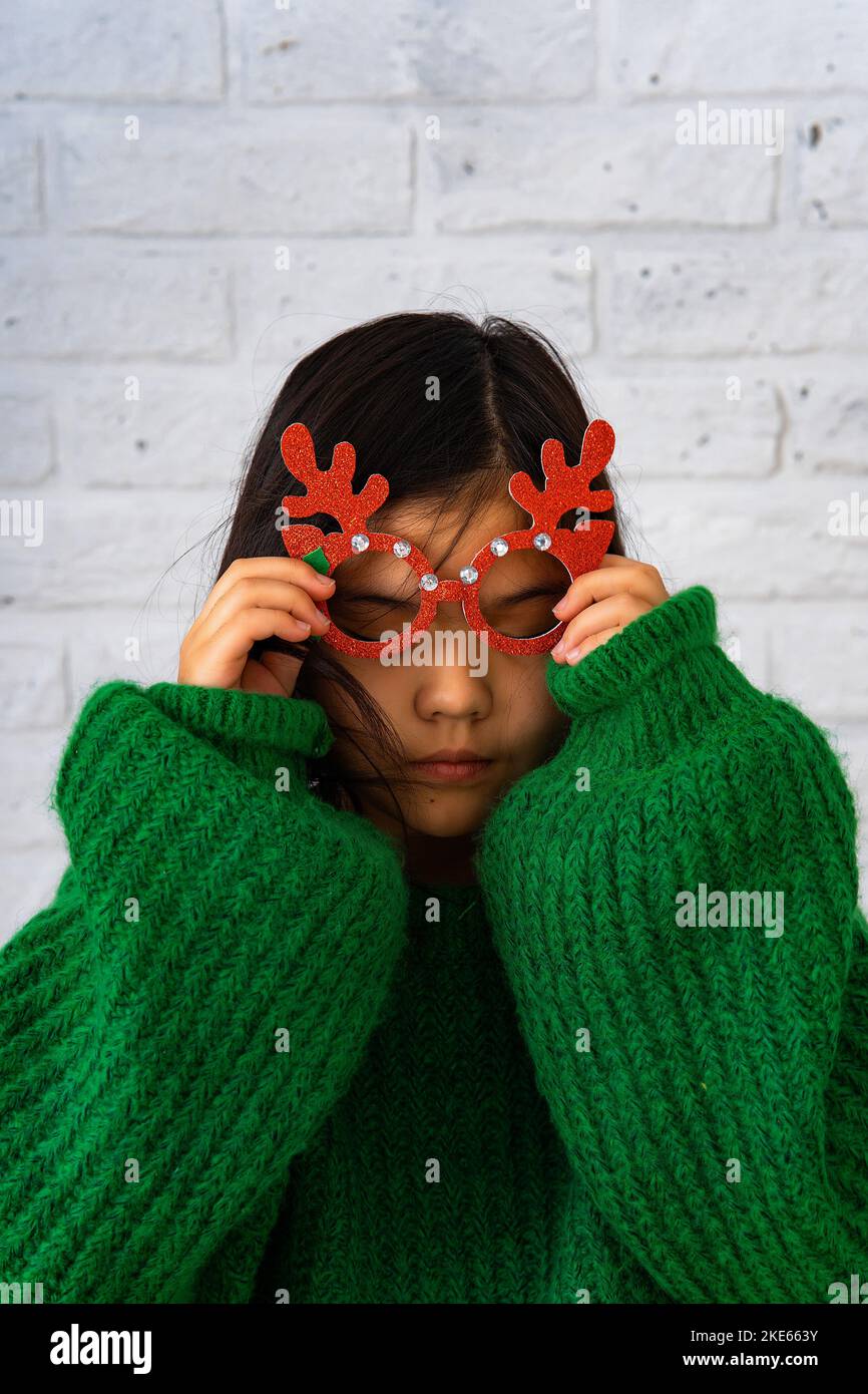 An Asian girl in a green sweater puts on masquerade glasses with deer horns Stock Photo