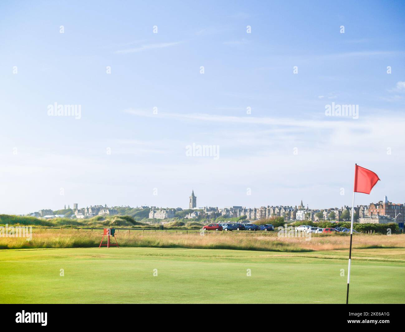Red hole flag on golf course with urban skyline behind at St Andrews