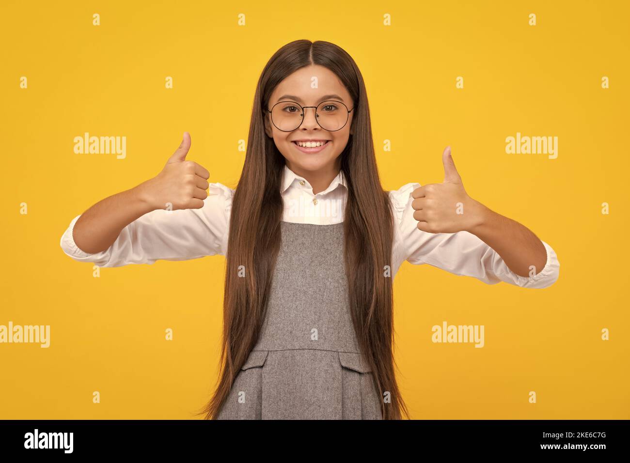 Optimistic cool teenager child girl with thumb up isolated on yellow background. Little schoolgirl student. Happy girl face, positive and smiling Stock Photo