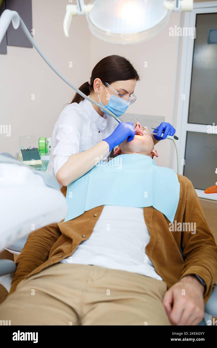 A female dentist treats tooth decay on a male patient's teeth at a dental clinic during the coronavirus pandemic. Selective focus Stock Photo