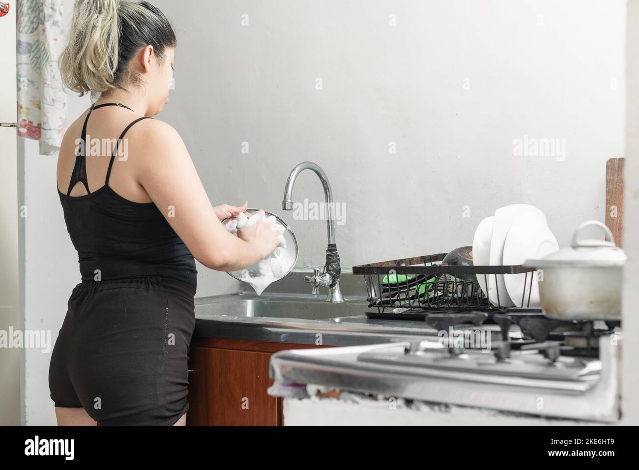 back view of a latina girl washing dishes in a dishwasher after