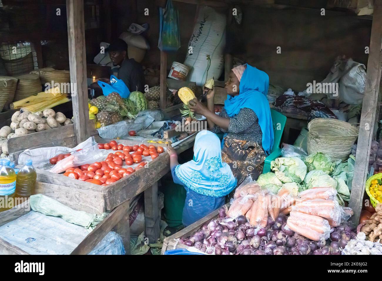 Mtowambu, Tanzania - October 12th, 2022: A market vendor peeling a pineapple, as her daughter watches. Stock Photo