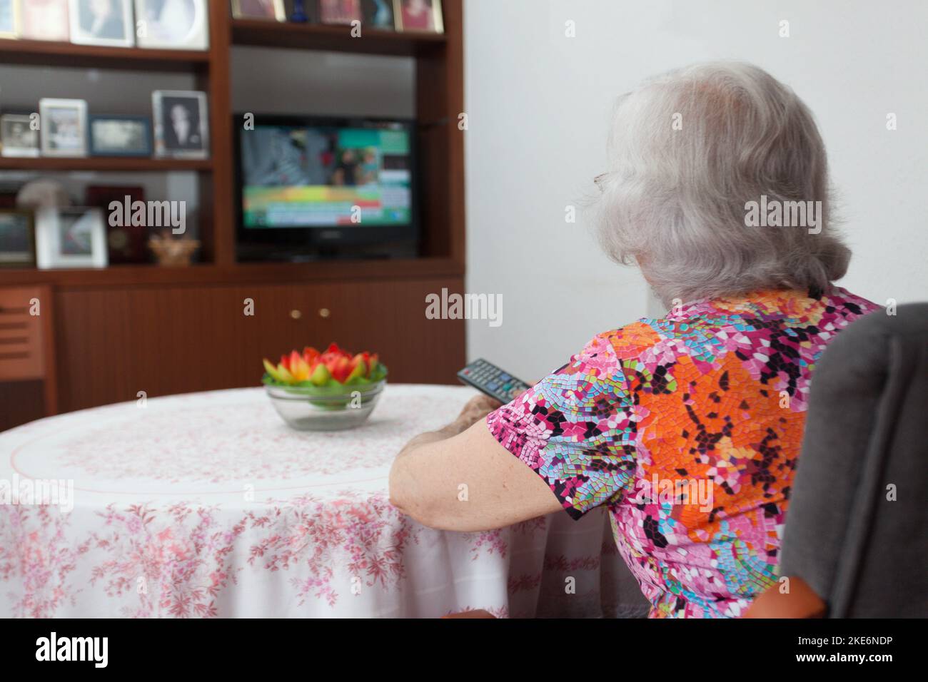 older white-haired woman watching TV in her living room, loneliness of the elderly, connectivity with the outside world. Stock Photo