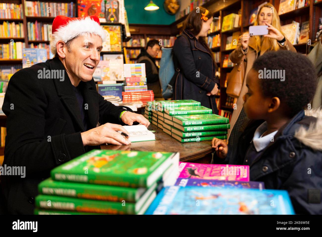 EDITORIAL USE ONLY Ben Miller signs a book for Kiyan Yearwood aged 4 from St Vincent's School at Daunt Books during Marylebone Village's 'Merry Marylebone' Christmas light switch on event, in support of mental health charity partner, Mind in Brent, Wandsworth and Westminster. Picture date: Thursday November 10, 2022. Stock Photo