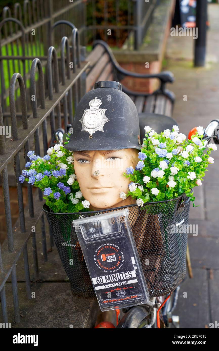 Dummy head wearing a Policeman's helmet in a basket on a bicycle with flowers advertising a local business Stock Photo