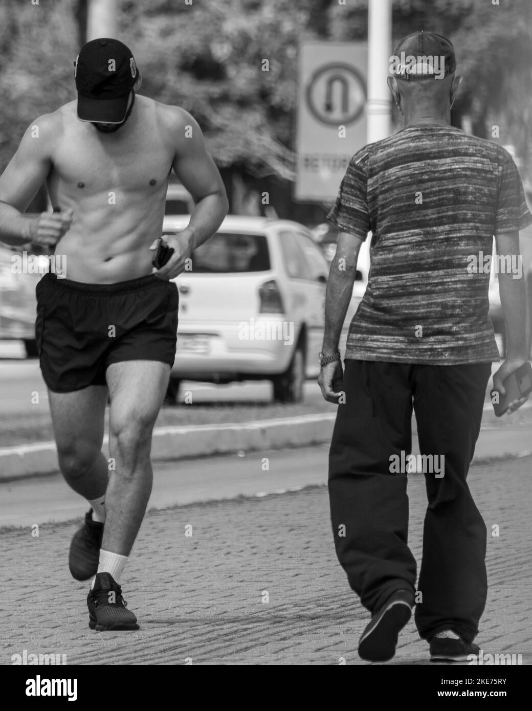 A greyscale shot of a young jogger and a senior person in a street Stock Photo