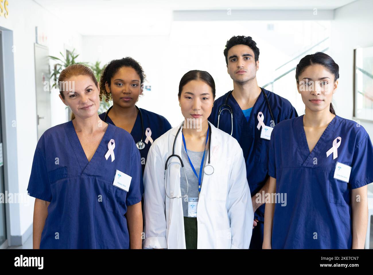 Portrait of diverse group of healthcare workers wearing cancer ribbons standing in hospital corridor Stock Photo