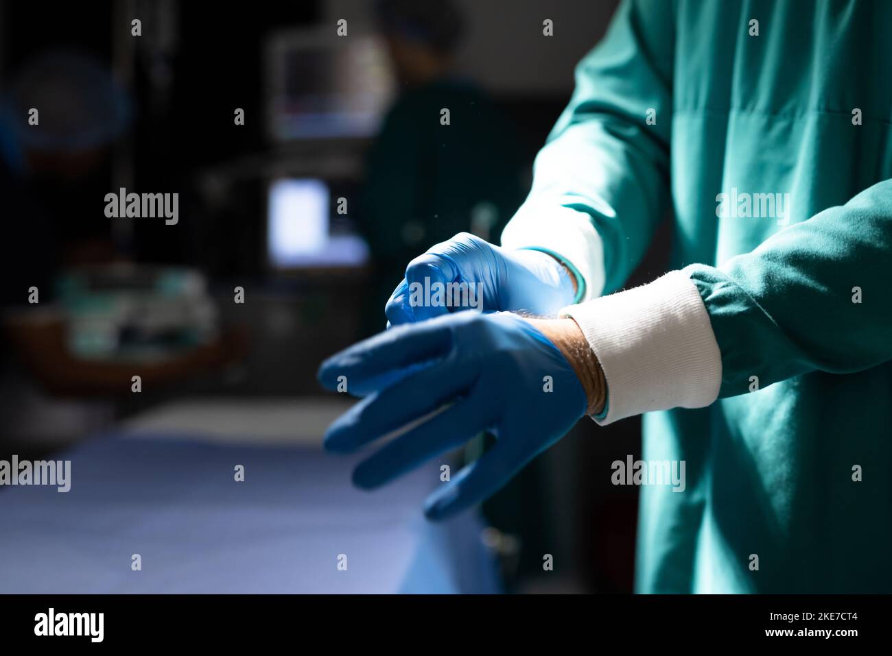 Midsection of surgeon putting on gloves in dark operating theatre, with copy space Stock Photo