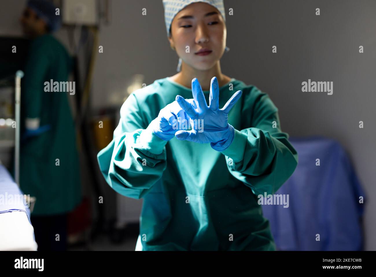 Asian female surgeon in surgical cap and gown putting on gloves in operating theatre Stock Photo