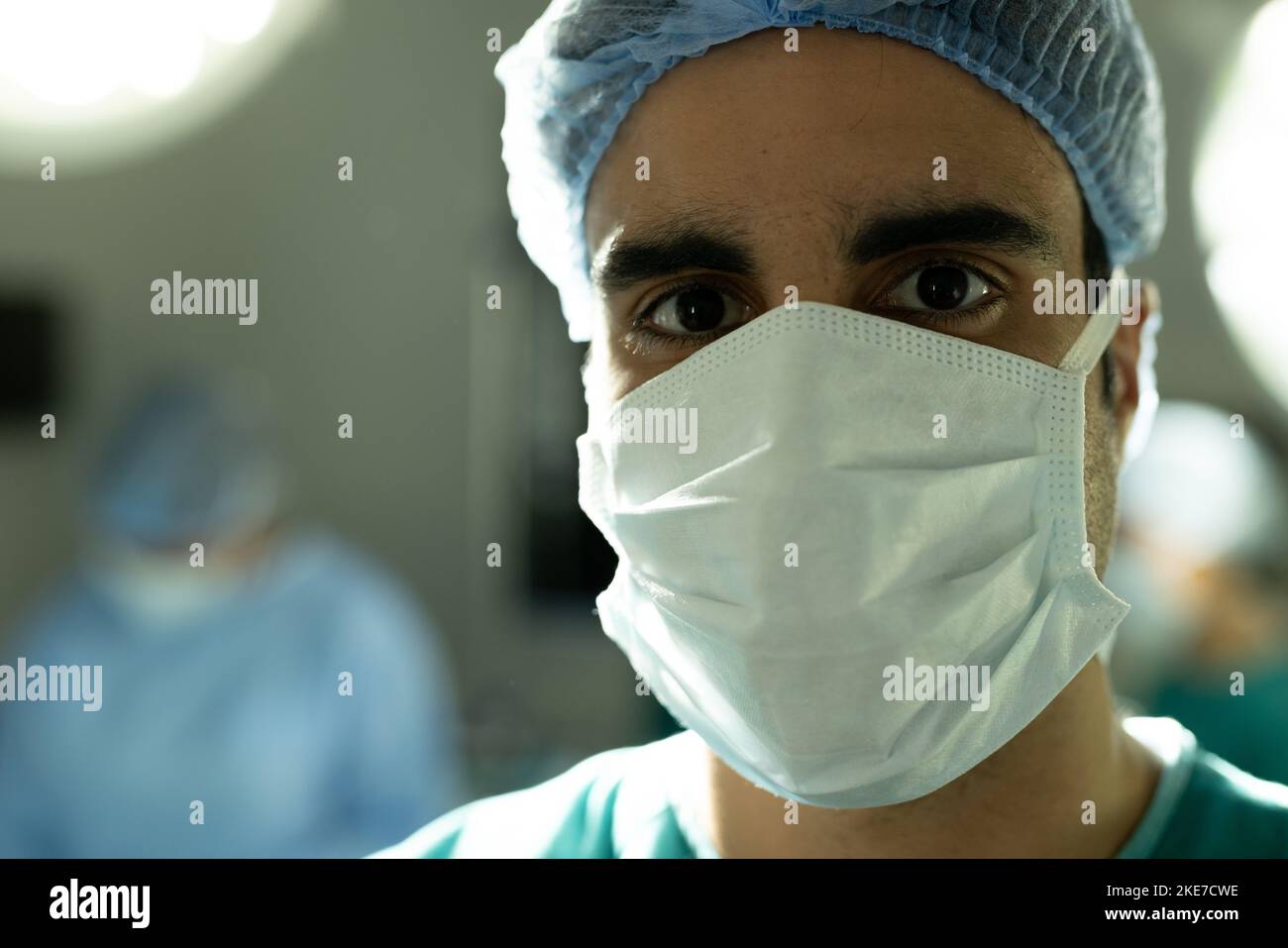 Portrait of biracial male surgeon in surgical cap and mask in operating ...