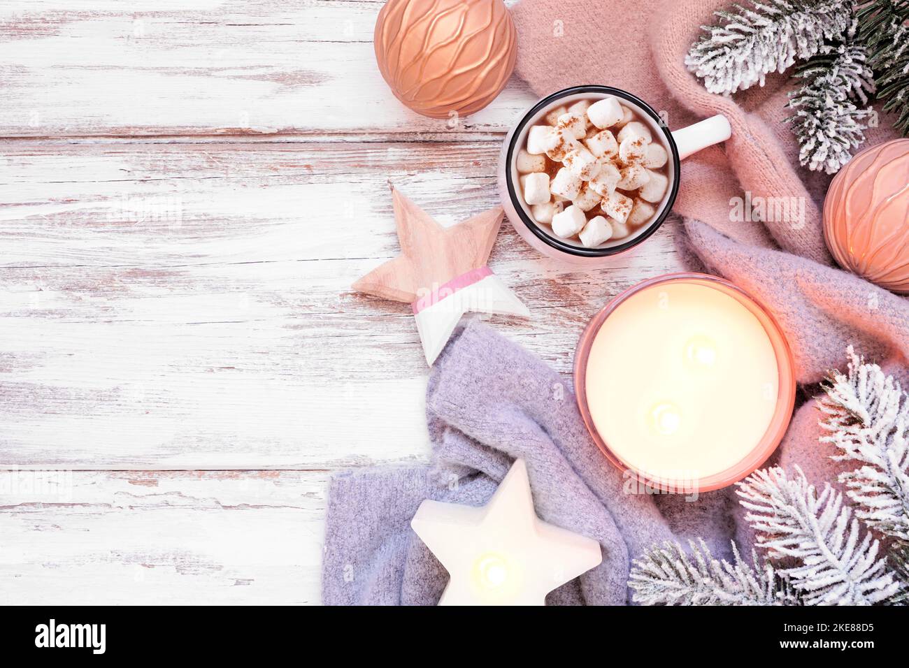 Cozy Christmas or winter side border with grey and dusty pink sweater, candle, hot chocolate, snowy branches and decor. Above view over a rustic white Stock Photo